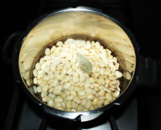 In the pressure cooker add the soaked beans, bay leaf and salt 